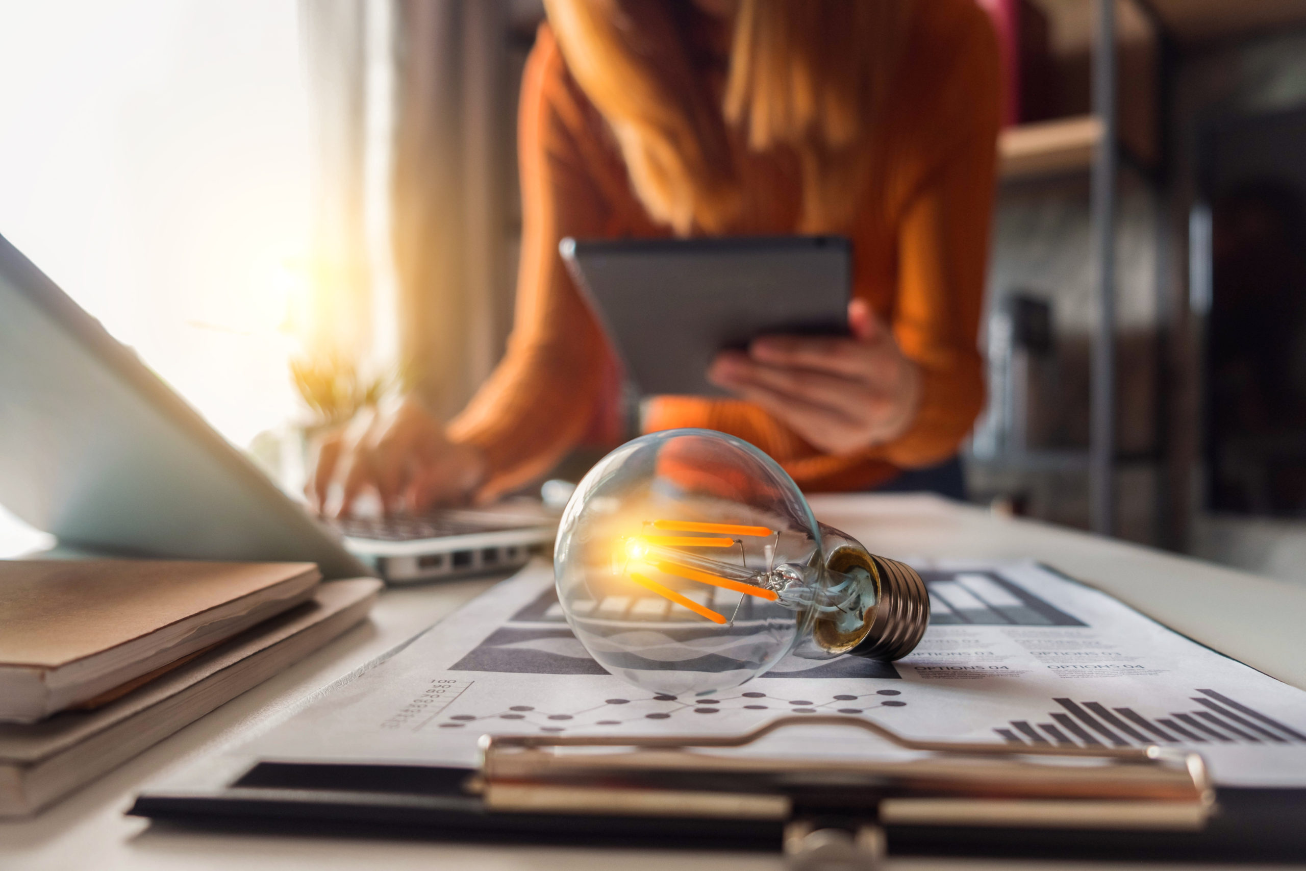 Young professional working on laptop with light bulb on her desk