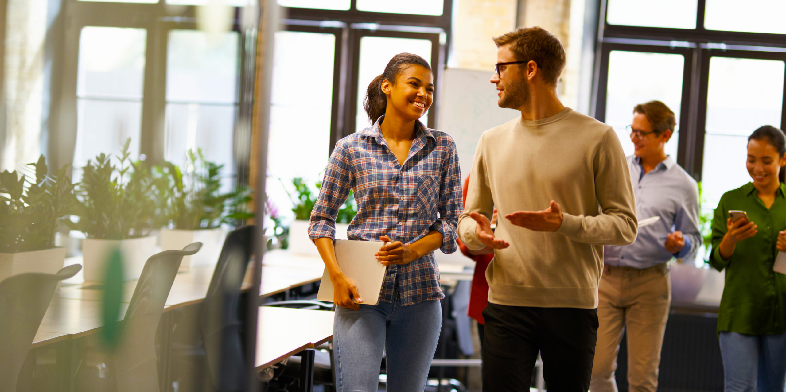 Two young diverse business people, male and female coworkers talking, discussing project and smiling while walking down the modern office