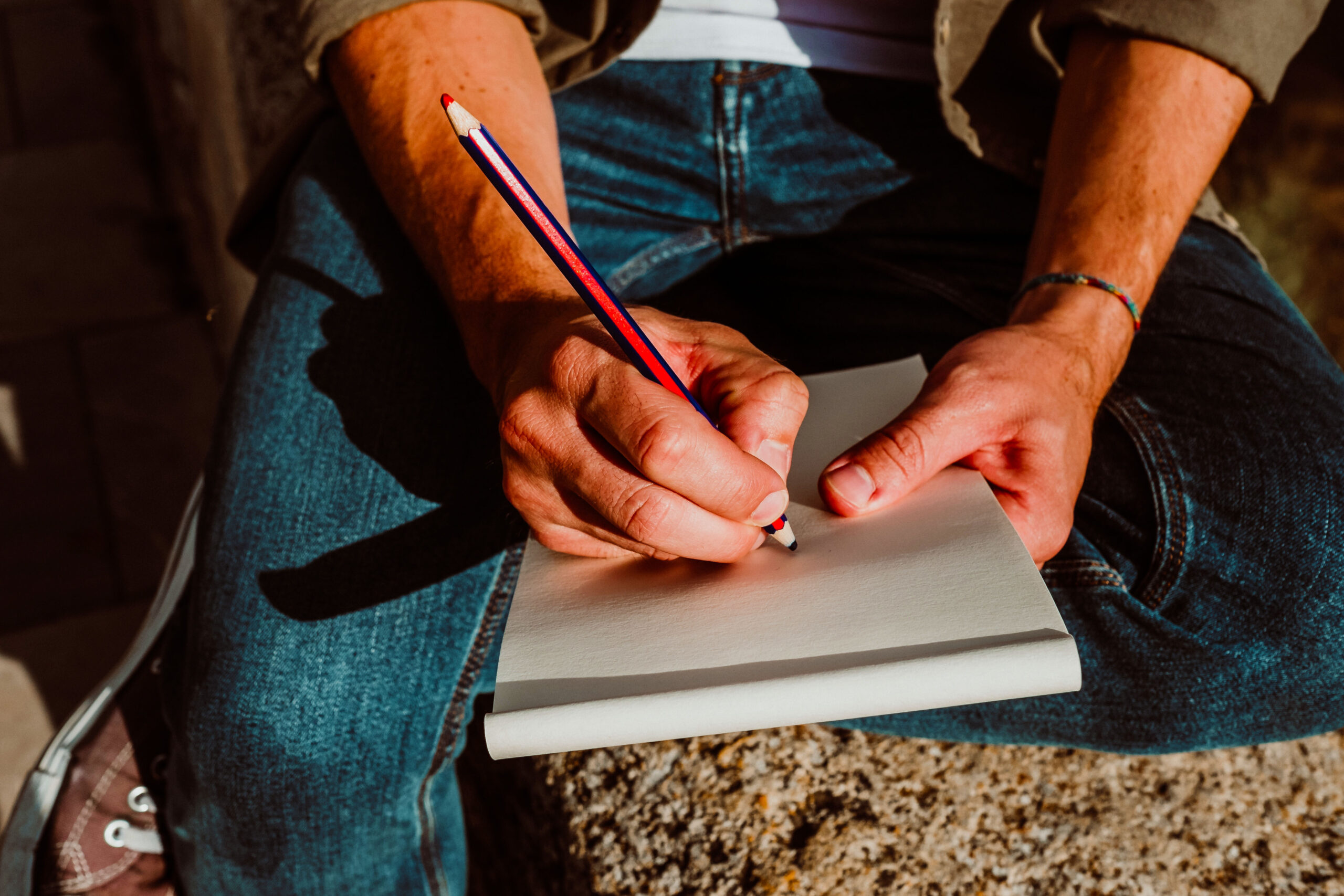 Young man sitting in the street of Granada, Spain, drawing in his travel notebook. Enjoying the sunset, developing his creativity. Relaxed and carefree. Lifestyle. Close up